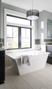 A modern bathroom with a tub that has two windows over it.
