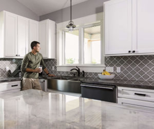 A man stands with a cup of coffee looking out a slider window in a modern kitchen.