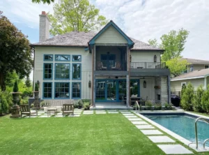 Modern home with expansive glass windows and sliding glass doors, green lawn, and inground pool