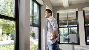 Man standing inside a house and looking out through single-hung windows