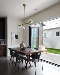 A wood dining table sits in front of a patio with black bifold doors open to enjoy the fresh air
